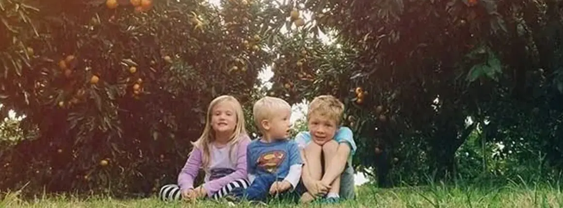 Three children sitting in the grass under a tree.